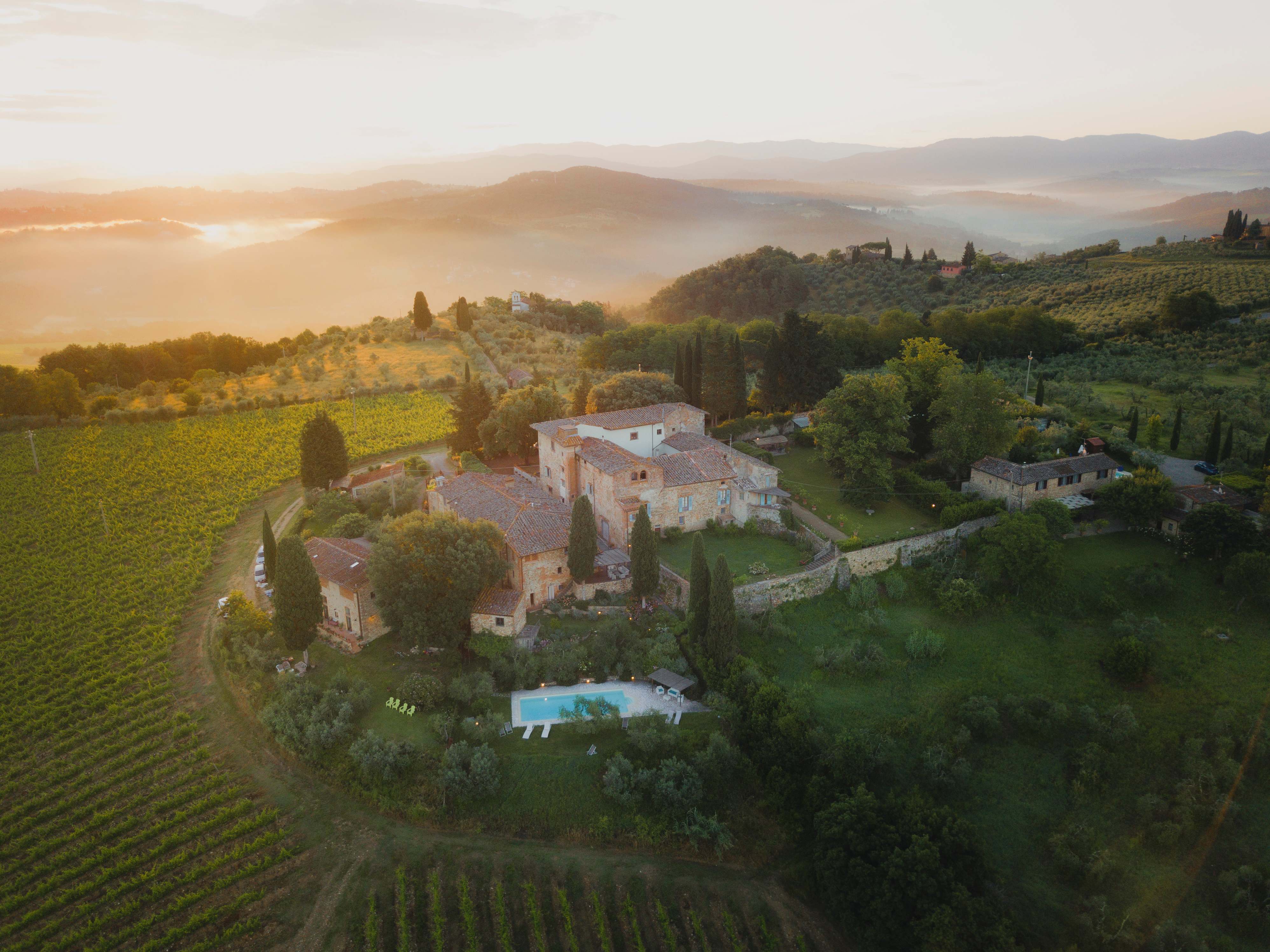 Aerial view of a Tuscan villa retreat surrounded by vineyards and cypress trees at golden hour